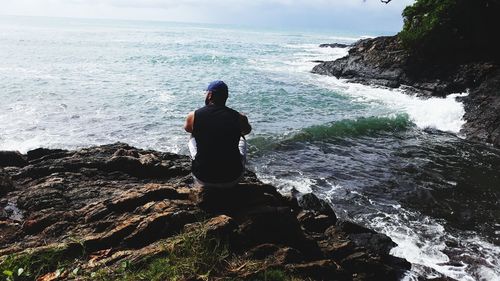 Rear view of man sitting on rocks by sea