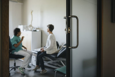 Doctor discussing with patient seen through doorway in hospital