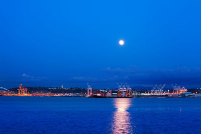 Sea by illuminated city against sky at night