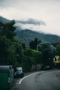 Cars on road by trees against sky during rainy season