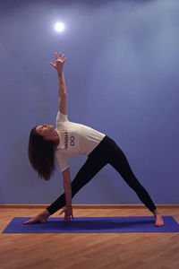 Woman practicing yoga against purple wall