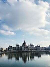 Reflection of building on river against cloudy sky