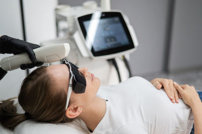 Young caucasian woman in goggles on photorejuvenation procedure. portrait of a girl in a beautician