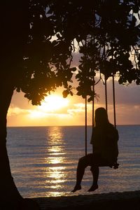 Silhouette man sitting on beach against sky during sunset