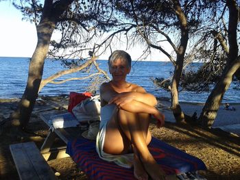 Full length of woman sitting on shore at beach against sky