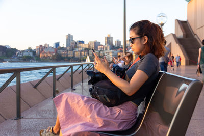 Woman using mobile phone while sitting on bench 