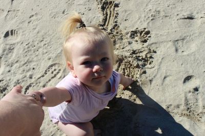 Cropped hand of person holding girl on sandy beach