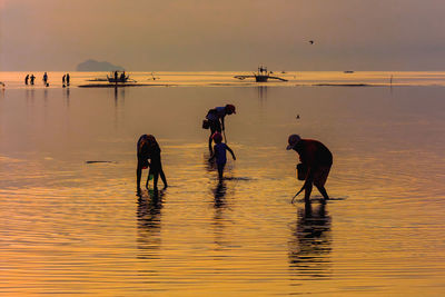 People on beach against sky during sunset