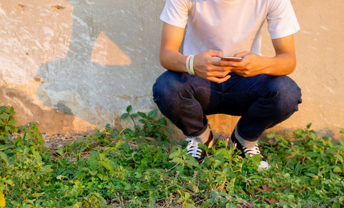 Low section of man using mobile phone while crouching on plants