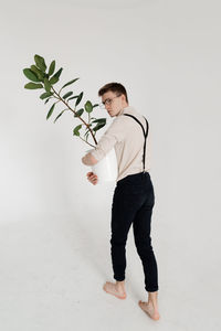 Young man with potted plant standing against white background