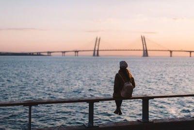 Alone dreamy unrecognizable girl sitting on edge of the sea. female watching at colorful sunset.