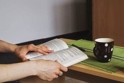 Cropped hands holding book by cup at table