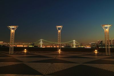 Lights on promenade with illuminated rainbow bridge in background at dusk