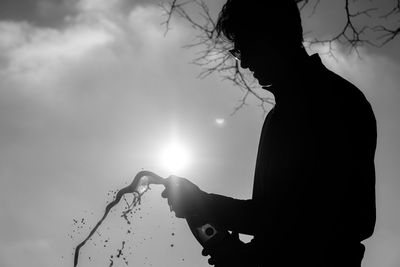 Silhouette man popping champagne while standing against sky on sunny day