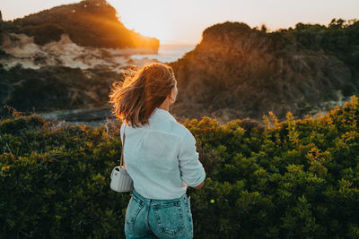 Rear view of woman standing on rock against sky