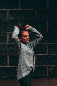 Moody portrait of girl who looks away from camera, standing against brick wall.