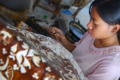 High angle view of mature woman doing design on batik at home