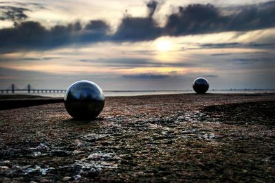 Spherical shaped sculptures on walkway against river at sunset