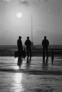 Silhouette men fishing on beach against sky