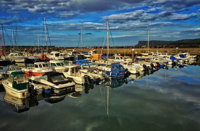 Boats in harbor against cloudy sky