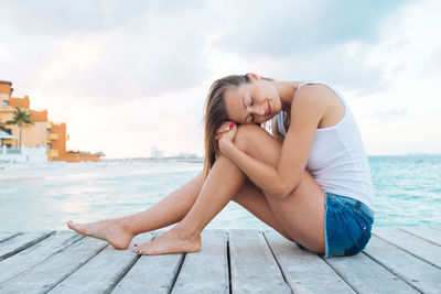 Young woman sitting on sea shore against sky