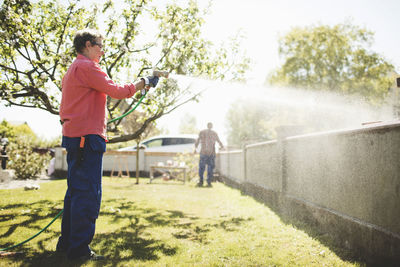 Side view of senior woman spraying water on concrete wall at yard