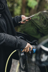 Midsection of man holding camera while standing by car