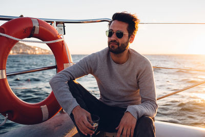 Young man sitting in boat on sea against sky