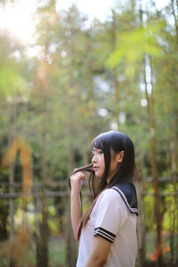 Side view of young woman standing against trees