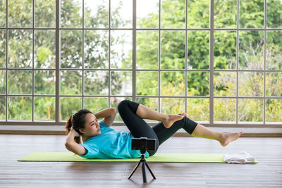 Sporty fit asian young woman doing bicycle crunch situp exercise lying on mat recorded by phone. 