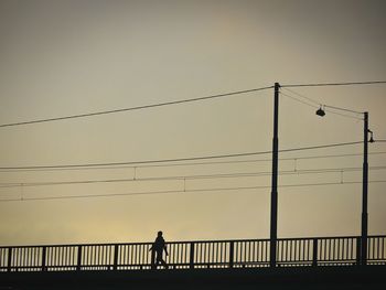 Low angle view of silhouette man walking on bridge against clear sky