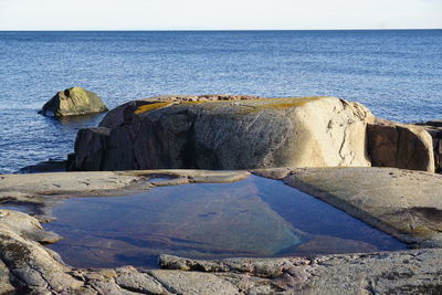 Scenic view of rock with standing water by sea against clear sky