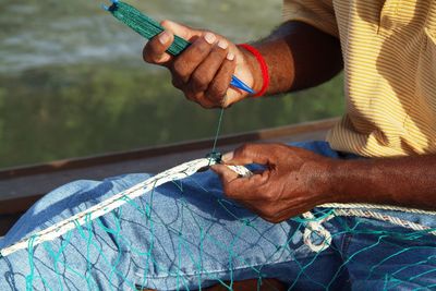 Mid section of a man stitching fishing net