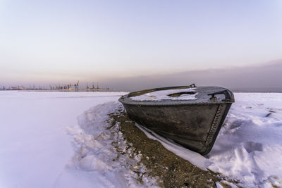 Snow covered boat on shore against sky during winter