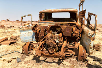 Abandoned rusty vehicle on field against sky