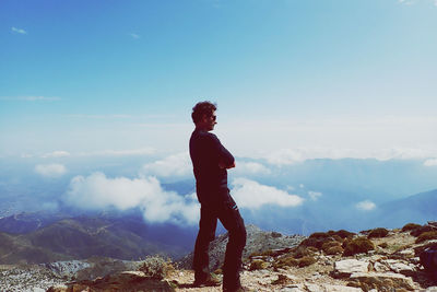 Man standing on rock looking at mountain against sky