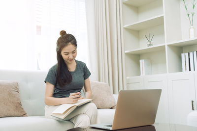 Young woman using phone while sitting on sofa