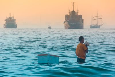 Rear view of man sitting in sea against sky