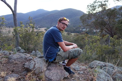 Young man sitting on rock against mountains
