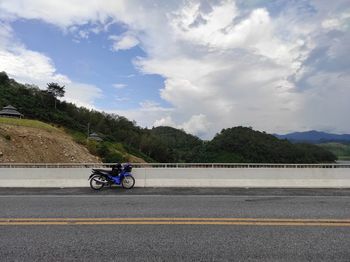 Man riding bicycle on road in city against sky