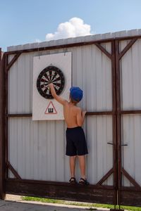 Rear view of boy holding dartboard on wall