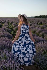 Rear view of woman with arms raised on field against sky