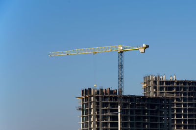 Low angle view of crane by building against clear blue sky