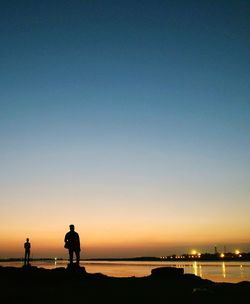 Silhouette men standing on shore against clear sky during sunset