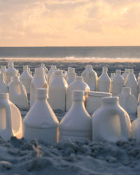 Close-up white gallons on beach against sky during sunset