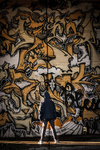 Rear view of man standing against graffiti wall