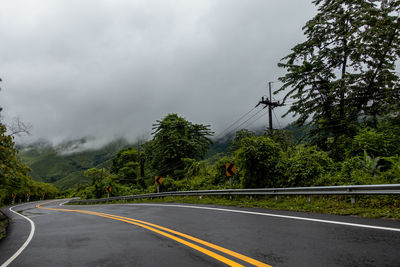 Road by trees against sky during rainy season