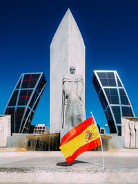 Low angle view of sculpture against building against clear blue sky