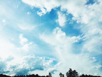 Low angle view of trees against cloudy sky