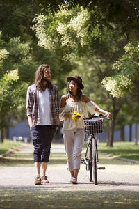 Full length of couple walking with bicycle on footpath at park